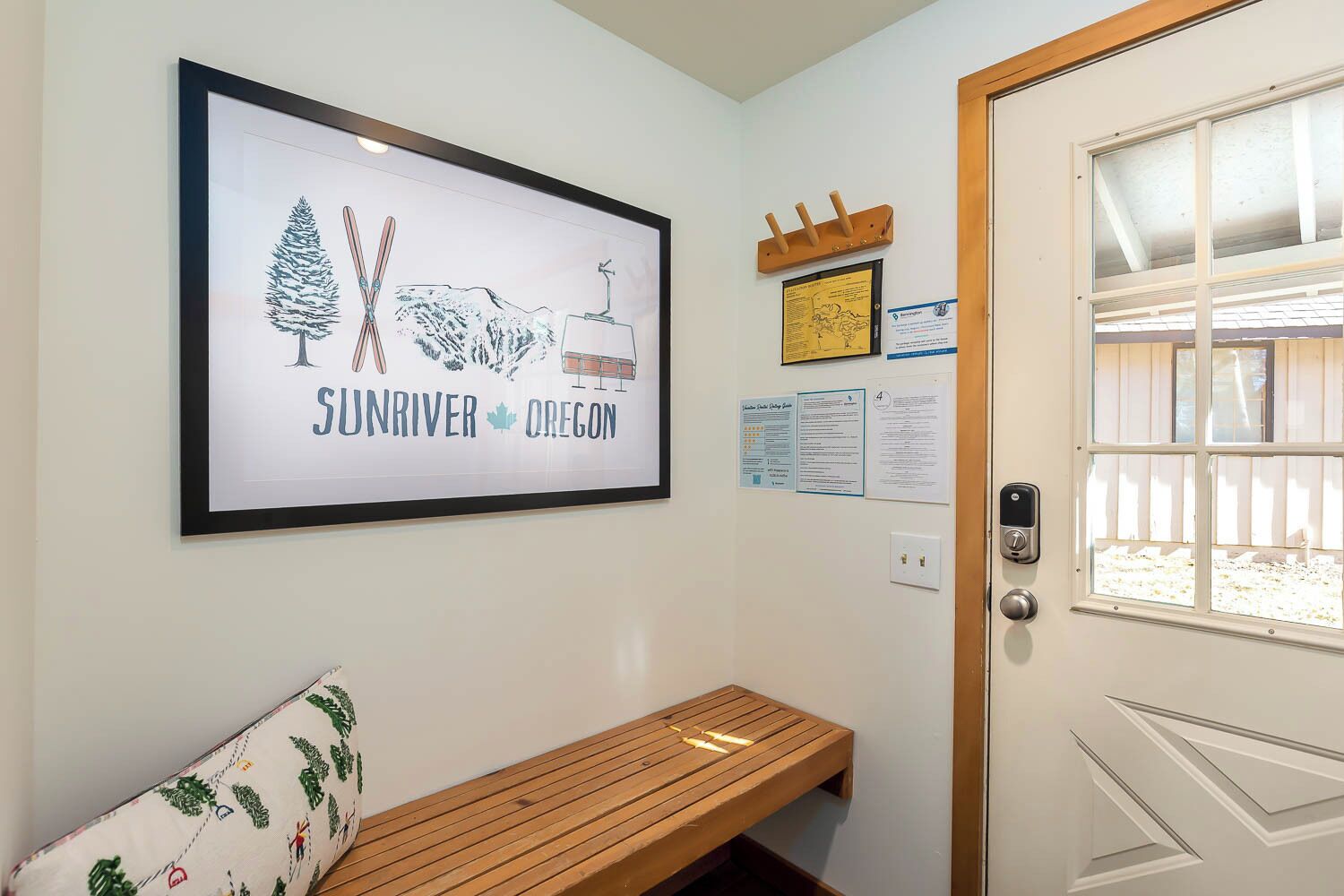 Un letrero en marco con el texto 'SUNRIVER OREGON', un banco de madera, una puerta con ventanal y un perchero en la pared.