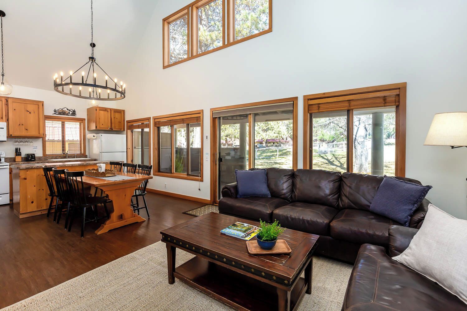 A spacious living area with a dining table, a leather sofa, and large windows offering a view of the outdoors.