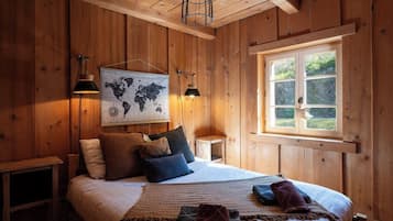 Una stanza con rivestimento in legno, un letto, due lampade a parete, una mappa del mondo e una finestra vista verde.