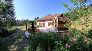 Una casa rústica amb teulada vermella, un gran canó de fusta i un jardí ple de flors roses.