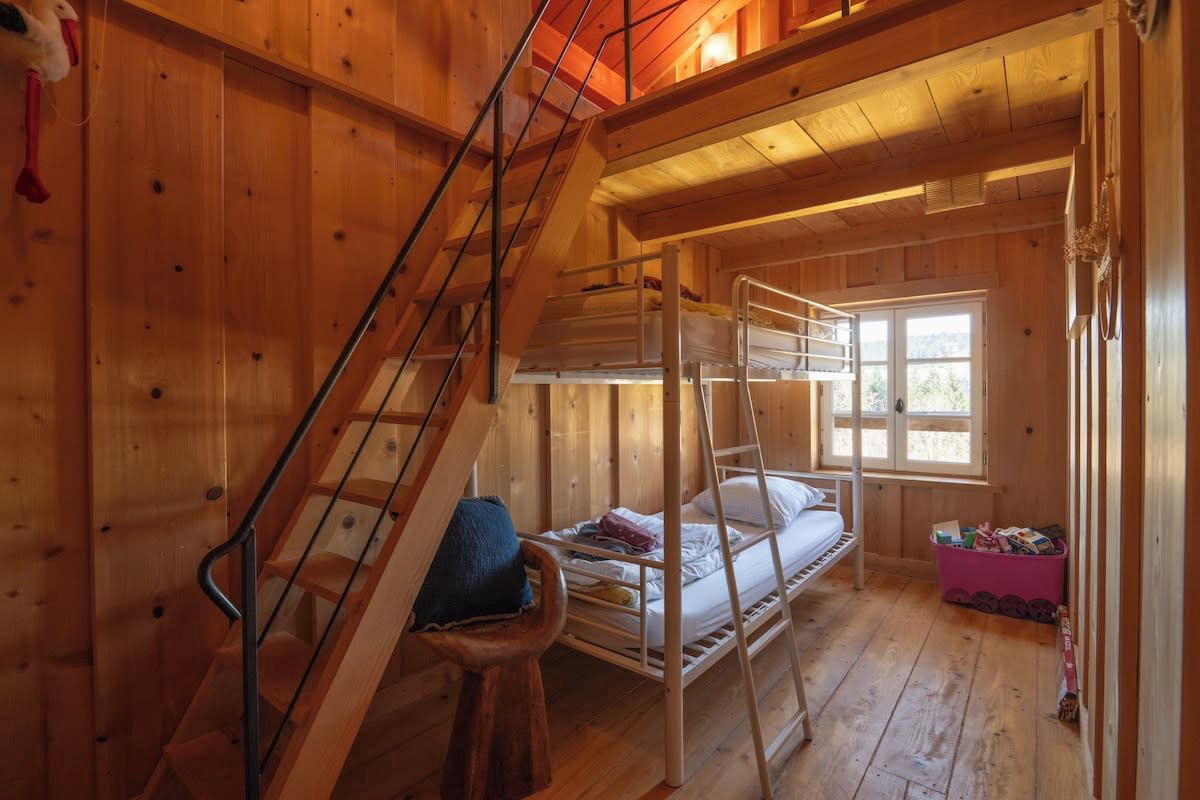 Ein Holzblockhaus-Interieur mit Etagenbetten, einer Treppe und einem Fenster.