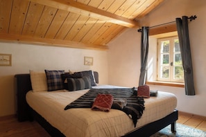A bedroom with a wooden ceiling, a bed with multiple pillows, a window with curtains, and a door.