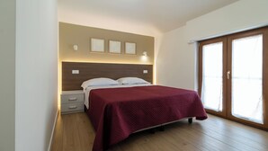 A bedroom with a bed, bedside tables, a wooden floor, and a large window with curtains.