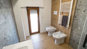 A modern bathroom with a wooden floor, a white toilet, a bidet, and a bathtub.