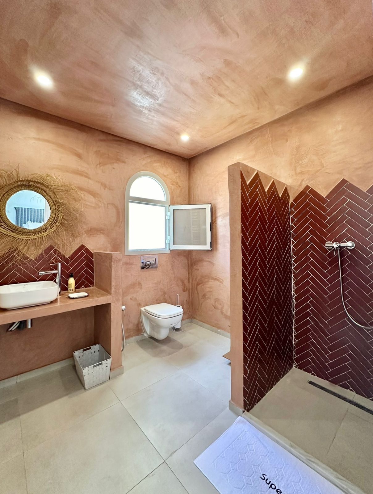 A bathroom with a sink, toilet, and shower area, featuring a herringbone tile pattern on the walls and a textured ceiling.