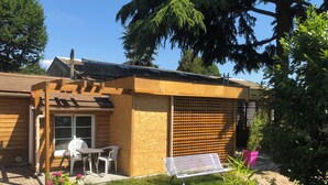 Une maison en bois avec un patio, une table et des chaises, et un jardin fleuri.