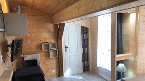 Un intérieur en bois comprenant un lit, une table, un téléviseur, une bibliothèque et une porte donnant sur une autre pièce.