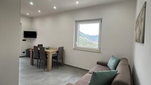 A modern living room with a sofa, dining table, chairs, a TV, and a large window with a view. - STILL HOUSE 1904 (San Nicola Arcella)
