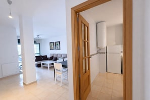 A modern living room with a sofa, a dining table, and a kitchen area with a refrigerator. - Apartamento en Rio Salado Conil (Conil de la frontera)