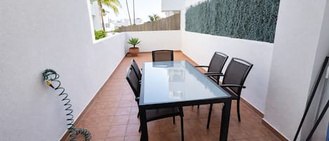 Un patio con una mesa y sillas de vidrio, rodeado de paredes blancas y un piso de baldosas.
