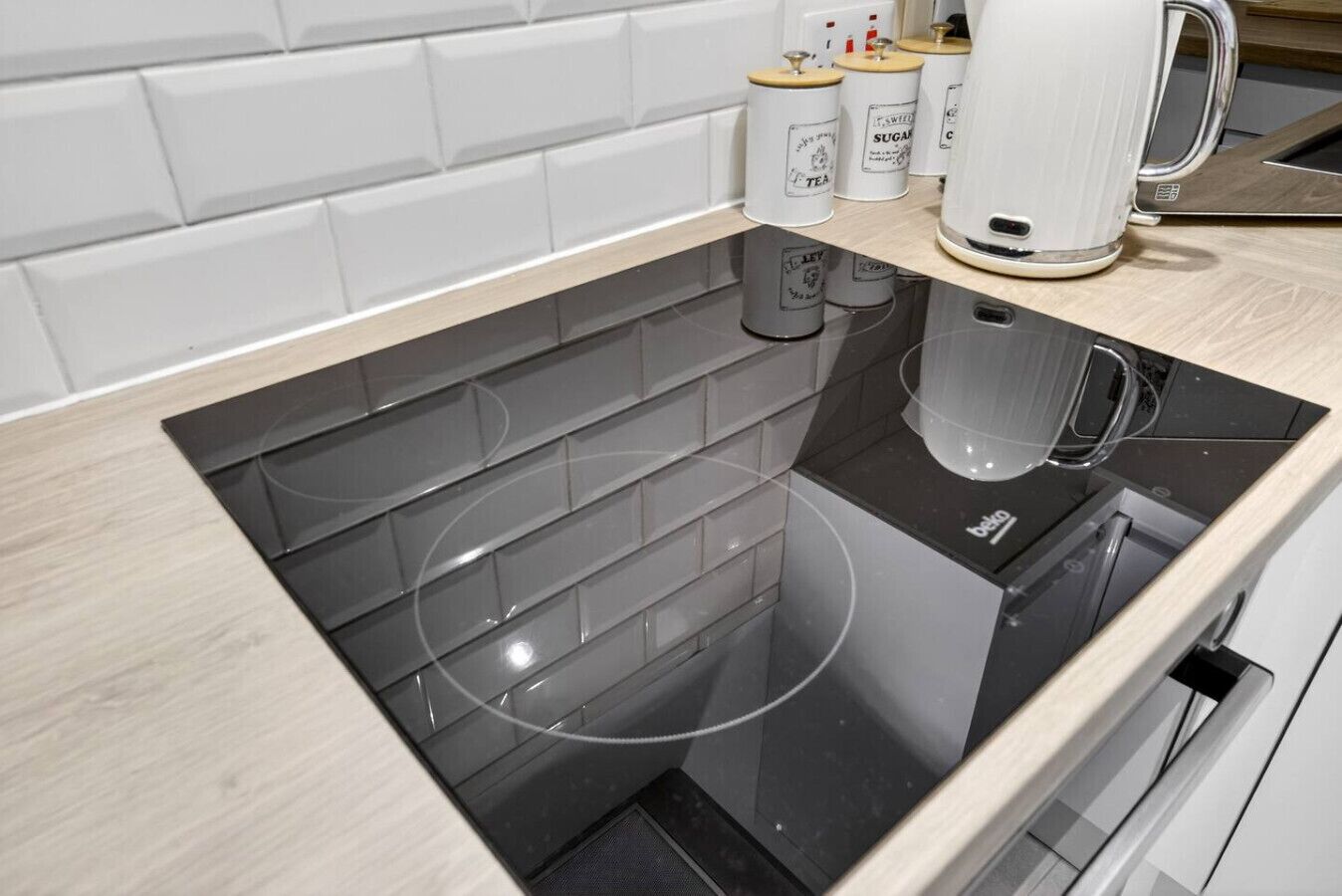 A kitchen with a black induction cooktop, white cabinets, and a white tiled backsplash.