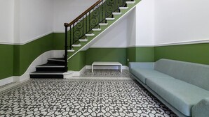 Un escalier avec une rampe noire, un banc blanc et un canapé bleu clair dans une pièce aux murs verts et au sol recouvert de carreaux décoratifs.