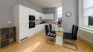 Une cuisine moderne avec des meubles blancs, un four noir et un coin repas comprenant une table en verre et des chaises noires.