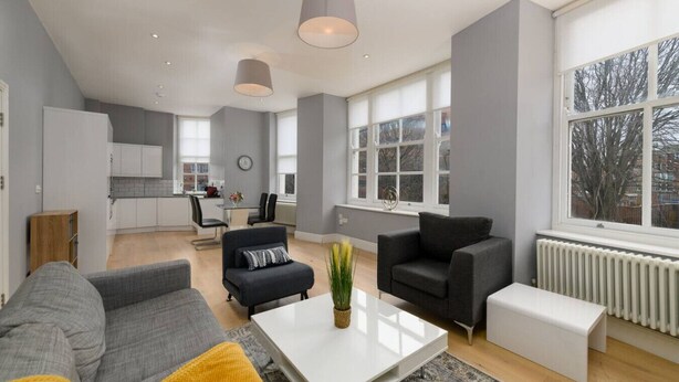 Un salon moderne comprenant un canapé, des fauteuils, une table basse et un coin repas avec une cuisine en arrière-plan.