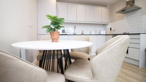 Una cucina moderna con mobili bianchi, un tavolo rotondo con sedie e una pianta in vaso.