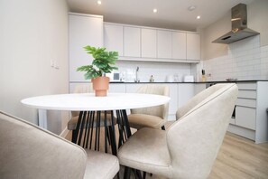 A modern kitchen with white cabinets, a round table with chairs, and a potted plant. - NEW! Elegant 2Bed City Living Near Cardiff Centre (Cardiff)