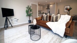 Ein modernes Wohnzimmer mit einer Couch, einem Fernseher, einer Pflanze und einer Küche im Hintergrund.