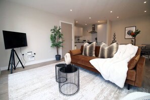 Ein modernes Wohnzimmer mit einer Couch, einem Fernseher, einer Pflanze und einer Küche im Hintergrund.