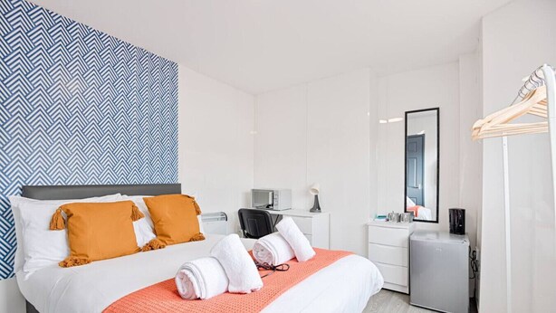 Quarto de hotel com cama, escrivaninha, cadeira, espelho e guarda-roupa.