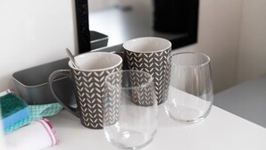 Uma mesa branca com três canecas estampadas, um copo de vidro transparente e um recipiente preto.