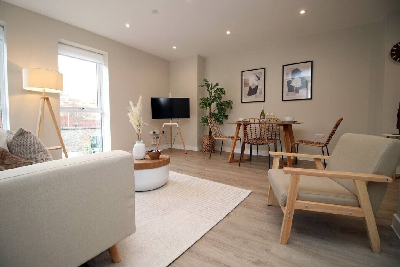 A modern living room with a sofa, a coffee table, a dining table with chairs, a TV, and artwork on the wall.