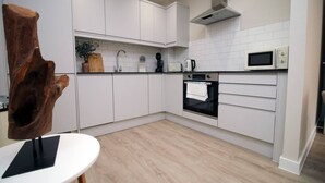 Una cucina moderna con mobili bianchi, forno integrato, microonde e una scultura in legno a sinistra.