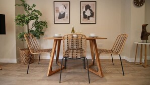 Zona pranzo con tavolo in legno e sedie in vimini, una pianta in vaso e due quadri astratti appesi al muro.