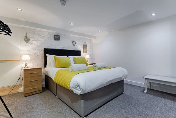 A modern bedroom with a bed, bedside tables, a bench, and a wall-mounted light fixture. - 1 Bed Home • Parking • Great for Contractors (Gorseinon)