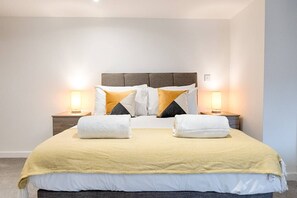 A neatly made bed with a headboard, two bedside tables with lamps, and a yellow throw blanket. - Contractor Base • Kitchen • Parking Included (Plasmarl)