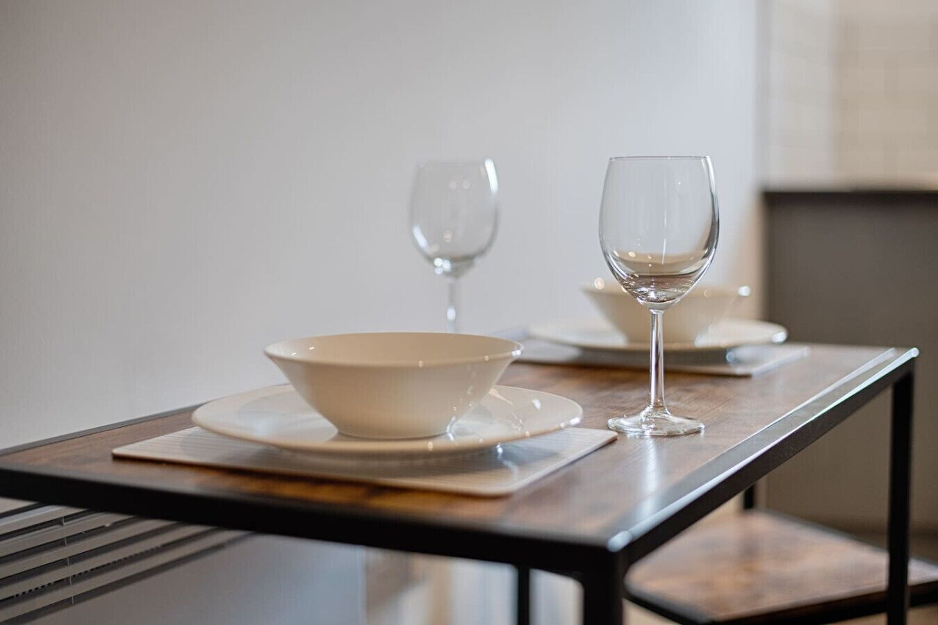 Une table à manger avec un saladier et deux verres à vin posés sur des sets de table.