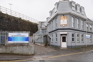 A grey building with a sign for KG Inspired Property, offering short stay accommodation, property maintenance, and property management.