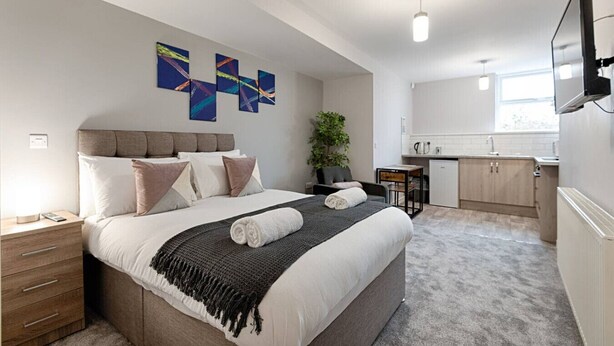 A modern hotel room with a large bed, a small desk, a kitchenette, and abstract wall art. - Contractor Base • Kitchen • Parking Included (Swansea)