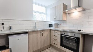 A modern kitchen with white cabinetry, a built-in oven, a microwave, and a dishwasher. - Contractor Base • Kitchen • Parking Included (Swansea)
