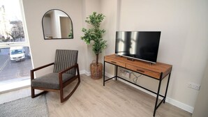A room with a wooden desk, a television, a chair, a mirror, and a potted plant. - NEW! Charming 2BR Home in a Popular Urban Quarter (Cardiff)