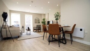 A modern living room with a sofa, a dining table with chairs, a tripod, and a large window. - NEW! Charming 2BR Home in a Popular Urban Quarter (Cardiff)