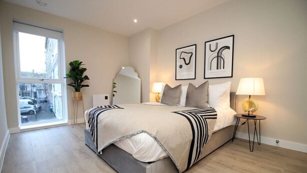 A modern bedroom with a large bed, bedside lamps, a window with a view, and two framed artworks on the wall. - NEW! Charming 2BR Home in a Popular Urban Quarter (Cardiff)