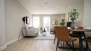 A modern living room with a sofa, a dining table with chairs, a floor lamp, and a potted plant. - NEW! Charming 2BR Home in a Popular Urban Quarter (Cardiff)