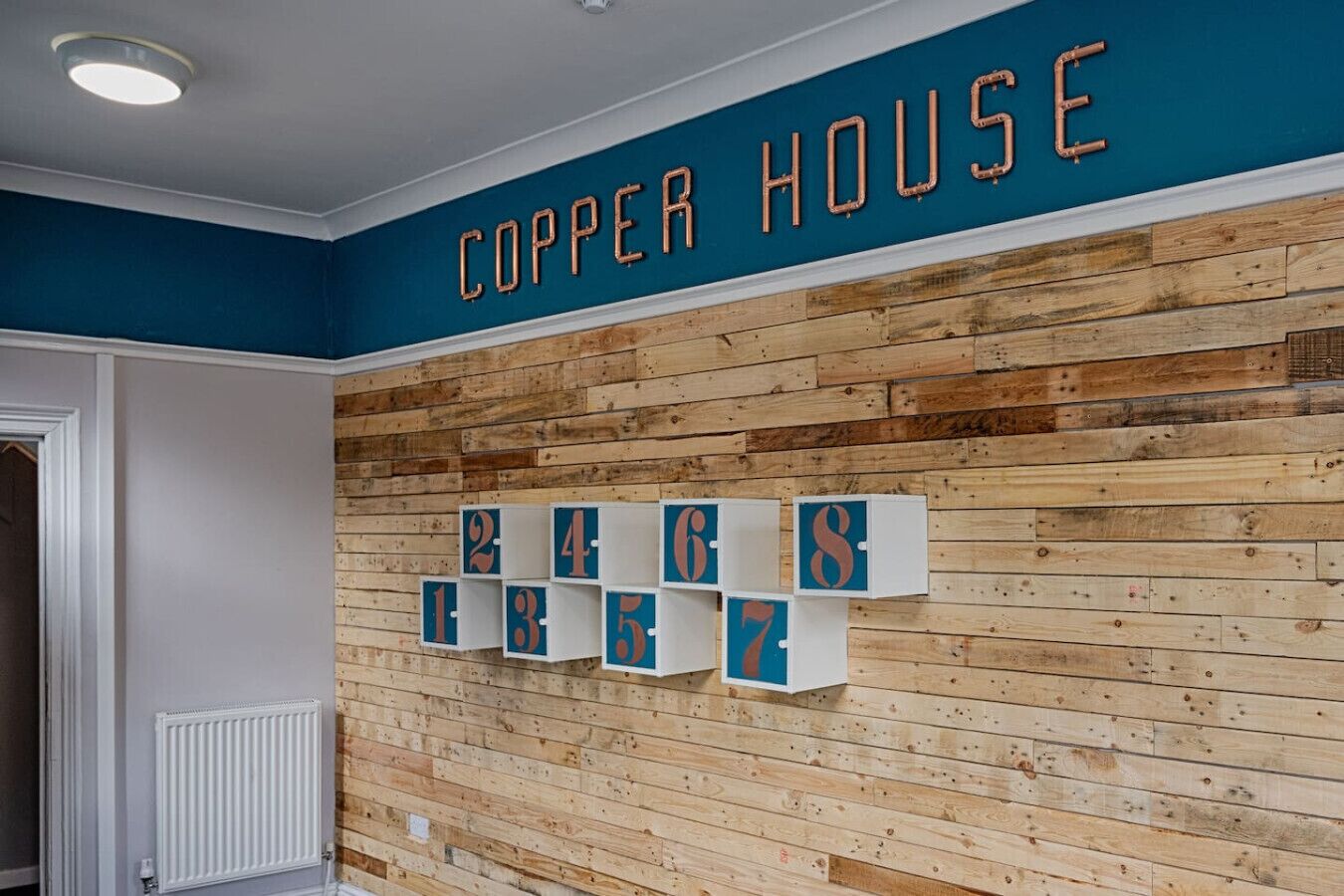 Une pièce avec un mur en bois, une enseigne indiquant « COPPER HOUSE », et des boîtes de rangement numérotées.