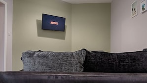 Een woonkamer met een donkerbruine bank, een flatscreen-televisie aan de muur en twee ingelijste foto's.