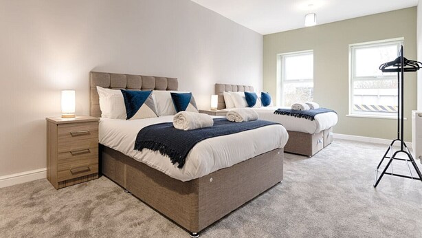 Een slaapkamer met twee bedden, een nachtkastje, een lamp en een staande lamp.