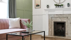 A living room with a sofa, a glass coffee table, a fireplace, and a green wall. - Pontcanna Paradise | 5 Mins to Centre | Fast Wifi (Pontcanna)