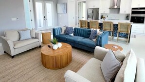 En moderne stue med sofa, sofabord og et køkkenområde med skabe og hårde hvidevarer.