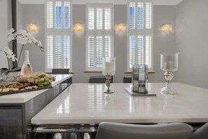 A dining area with a marble table, white chairs, a centerpiece with flowers, and decorative wall sconces. - Modern & Unique - Central & Beach Access (Swansea)