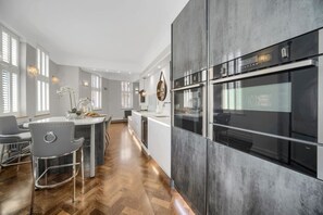 A modern kitchen with a central island, stainless steel appliances, and a herringbone wood floor. - Modern & Unique - Central & Beach Access (Swansea)