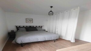 Un dormitorio con una cama, una mesita de noche, una lámpara colgante y un ventanal con cortinas.