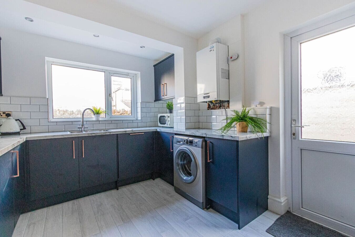A compact kitchen with a washing machine, a microwave, and a window providing natural light.