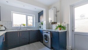 Cocina compacta con lavadora, microondas y ventana que deja entrar luz natural.