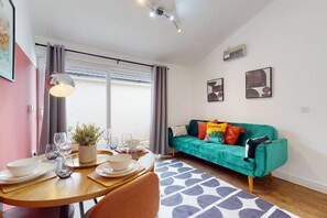 Ein Essbereich mit einem Tisch für vier Personen, einer Couch mit bunten Kissen und einem Fenster mit Vorhängen.