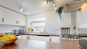 Una cucina moderna con mobili bianchi, un piano di lavoro in legno, un piano cottura integrato e una finestra che lascia entrare luce naturale.
