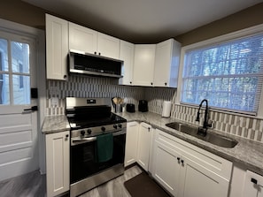 A modern kitchen with white cabinets, a stainless steel range, a built-in oven, a window with blinds, and a granite countertop. - Camel City Oasis * * Sleeps 8 * * Near Old Salem (Winston-Salem)